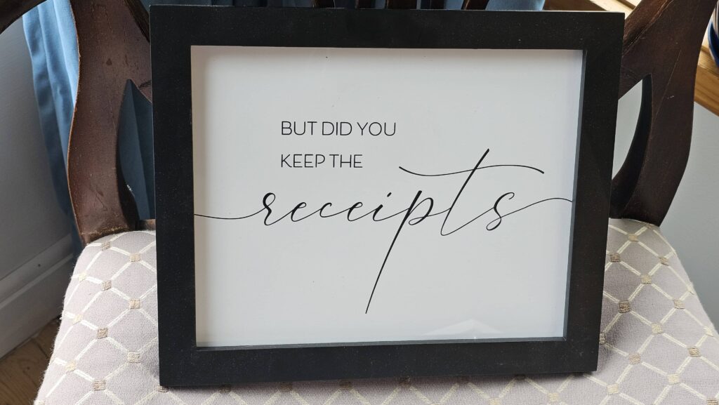 A framed quote on a patterned chair reads, "But did you keep the receipts," blending stylish script with modern decor in a cozy setting.