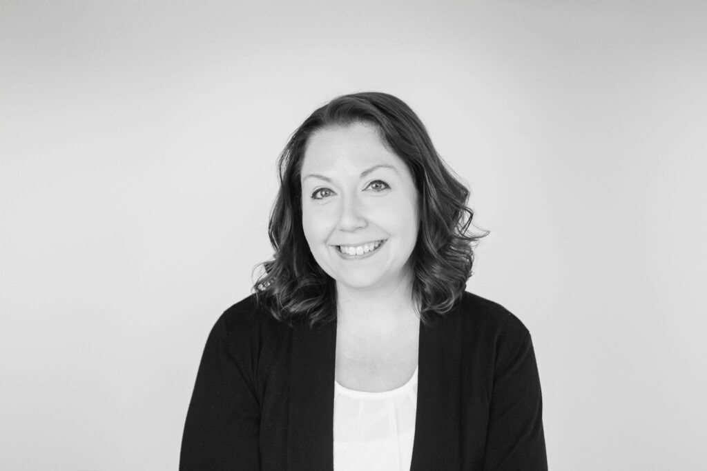 A person smiles in a black and white portrait against a plain background, wearing a dark cardigan and light blouse.